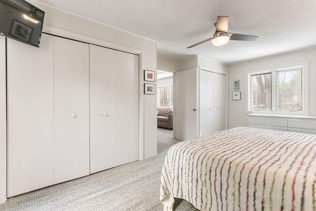 carpeted bedroom featuring two closets, a ceiling fan, and a textured ceiling