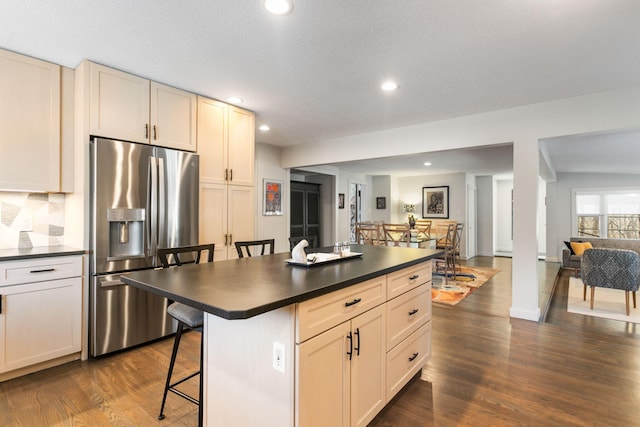 kitchen with dark countertops, recessed lighting, a kitchen breakfast bar, dark wood-style floors, and stainless steel fridge