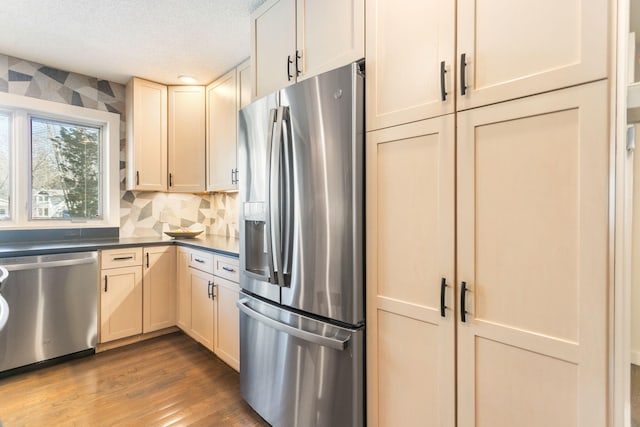 kitchen featuring dark countertops, a textured ceiling, wood finished floors, appliances with stainless steel finishes, and decorative backsplash