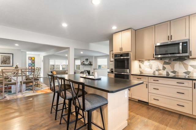 kitchen featuring a kitchen breakfast bar, dark countertops, dark wood finished floors, appliances with stainless steel finishes, and decorative backsplash