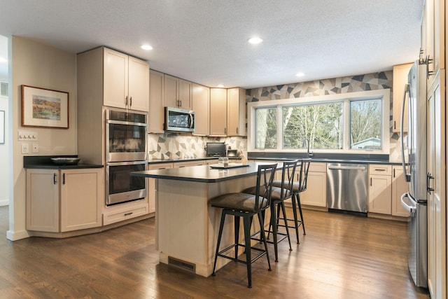 kitchen with a breakfast bar, dark wood finished floors, stainless steel appliances, dark countertops, and tasteful backsplash