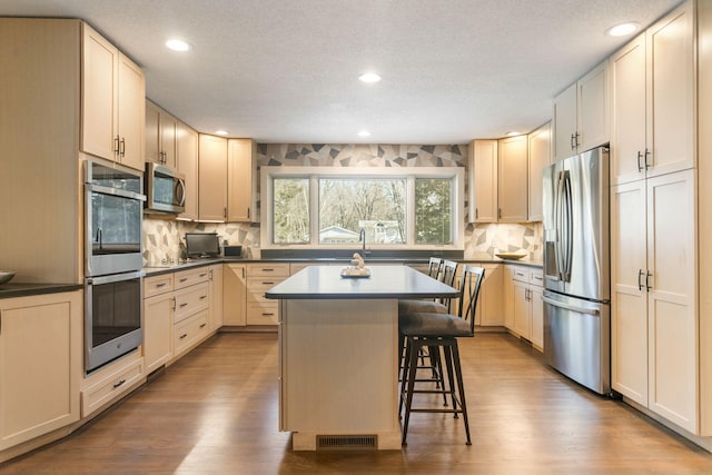 kitchen with a kitchen bar, appliances with stainless steel finishes, wood finished floors, and visible vents