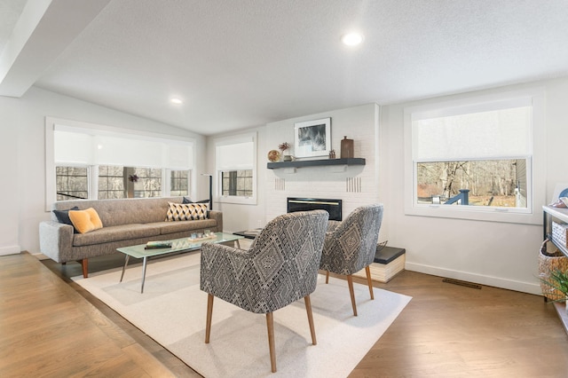 living area with wood finished floors, baseboards, lofted ceiling, a textured ceiling, and a brick fireplace