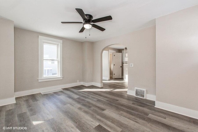 spare room featuring arched walkways, wood finished floors, visible vents, and baseboards