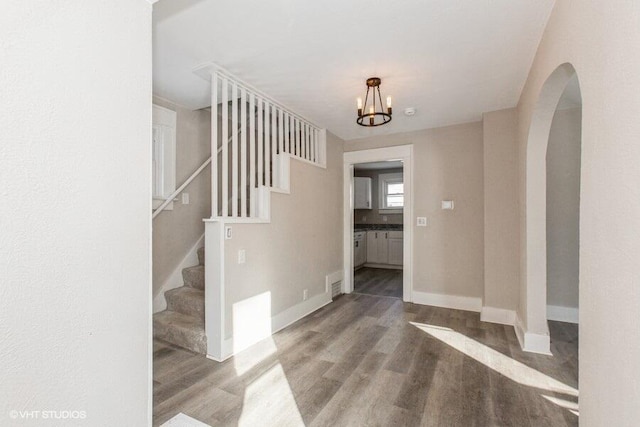 entryway with baseboards, arched walkways, wood finished floors, stairs, and a notable chandelier