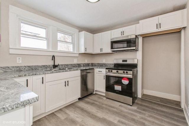 kitchen featuring light wood-style flooring, stainless steel appliances, a sink, white cabinetry, and light stone countertops