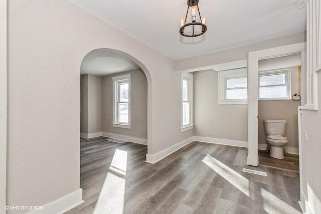 interior space with arched walkways, baseboards, and wood finished floors