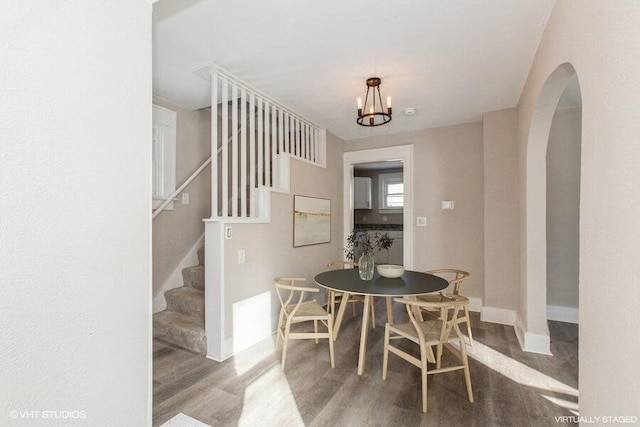 dining area with arched walkways, stairway, wood finished floors, a chandelier, and baseboards