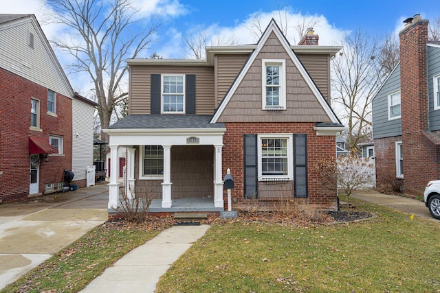 view of front of property featuring a porch, a chimney, a front lawn, and brick siding