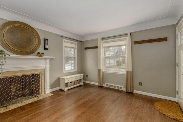 unfurnished living room featuring visible vents, plenty of natural light, a tiled fireplace, and wood finished floors