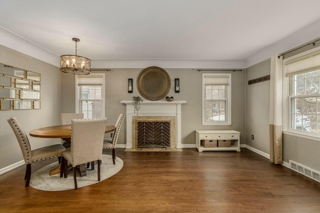 dining area with baseboards, visible vents, a tiled fireplace, wood finished floors, and a chandelier