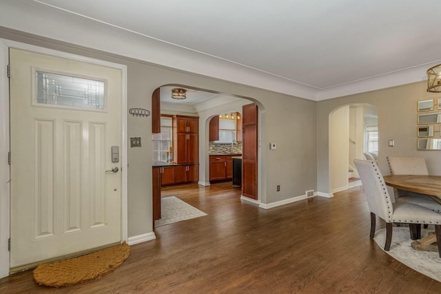 foyer featuring dark wood-style floors, baseboards, and arched walkways