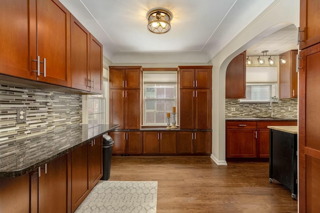 kitchen with arched walkways, dark wood-style flooring, brown cabinets, backsplash, and a sink