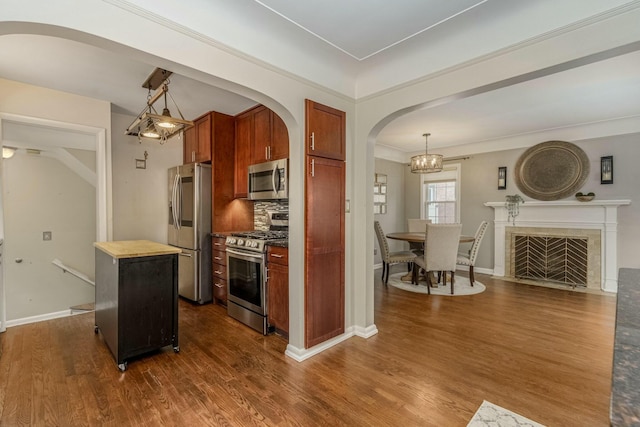 kitchen featuring dark wood-style floors, appliances with stainless steel finishes, a tiled fireplace, and backsplash