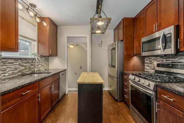 kitchen featuring dark stone counters, appliances with stainless steel finishes, dark wood-type flooring, and a sink