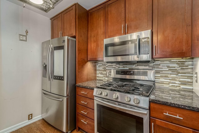 kitchen with baseboards, appliances with stainless steel finishes, backsplash, dark stone counters, and brown cabinetry