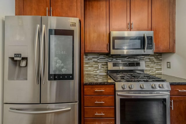 kitchen featuring stainless steel appliances, brown cabinets, dark stone countertops, and tasteful backsplash