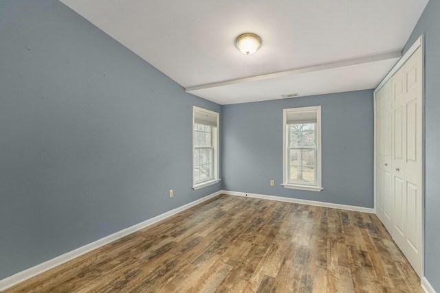 unfurnished bedroom featuring a closet, wood finished floors, visible vents, and baseboards