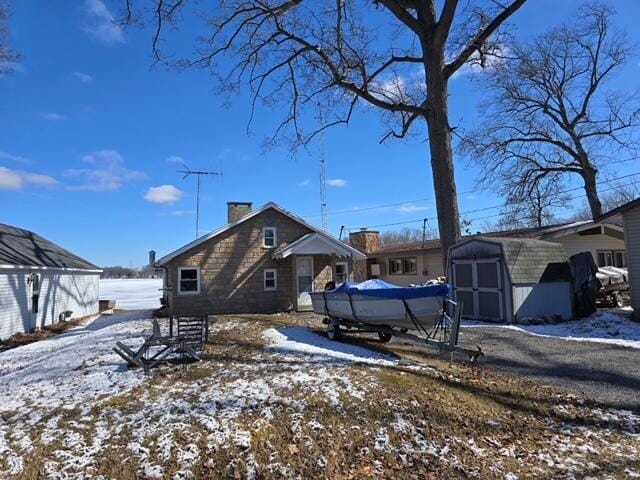 view of snowy exterior featuring a shed, a chimney, and an outbuilding