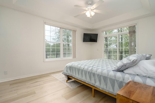 bedroom featuring ceiling fan, baseboards, access to outside, light wood-type flooring, and a tray ceiling