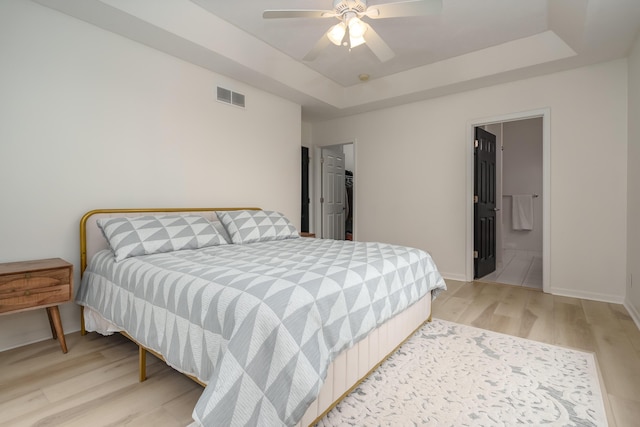 bedroom with baseboards, visible vents, ceiling fan, a tray ceiling, and light wood-style floors