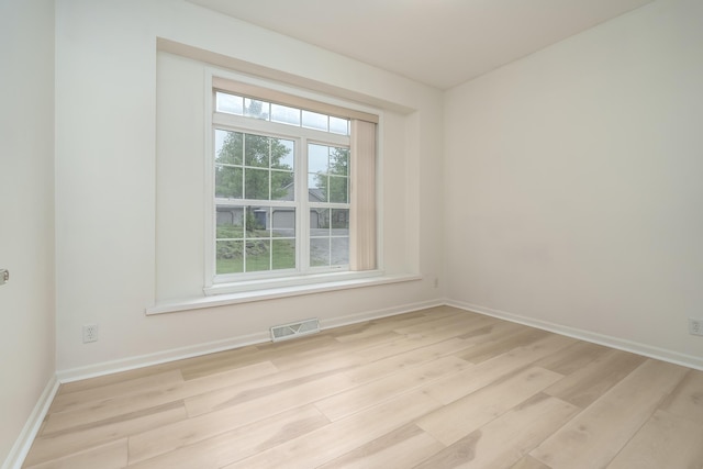 empty room with light wood-type flooring, visible vents, and baseboards