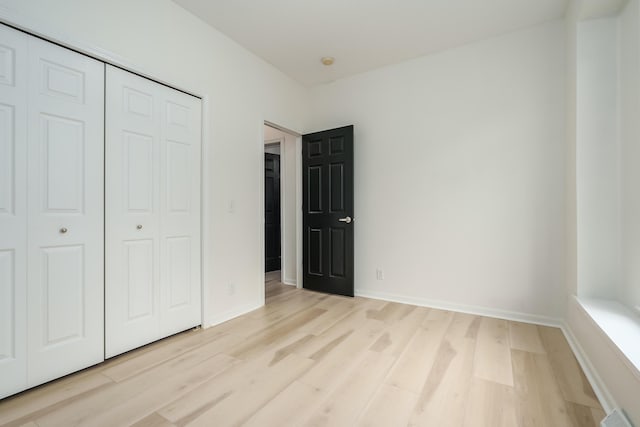 unfurnished bedroom featuring light wood-style floors, a closet, and baseboards