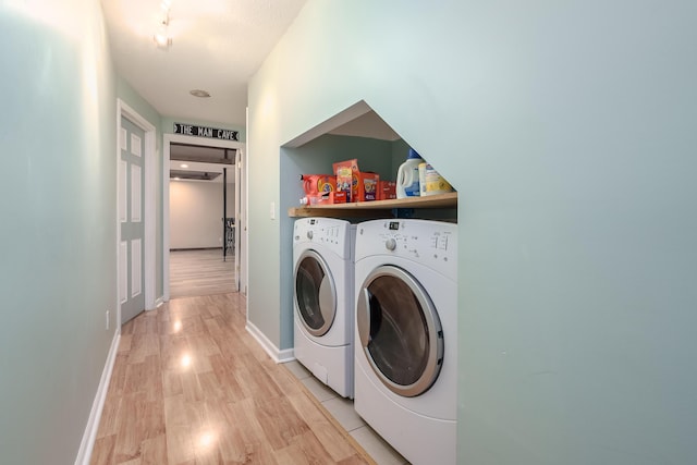 clothes washing area with laundry area, washing machine and dryer, light wood-style flooring, and baseboards