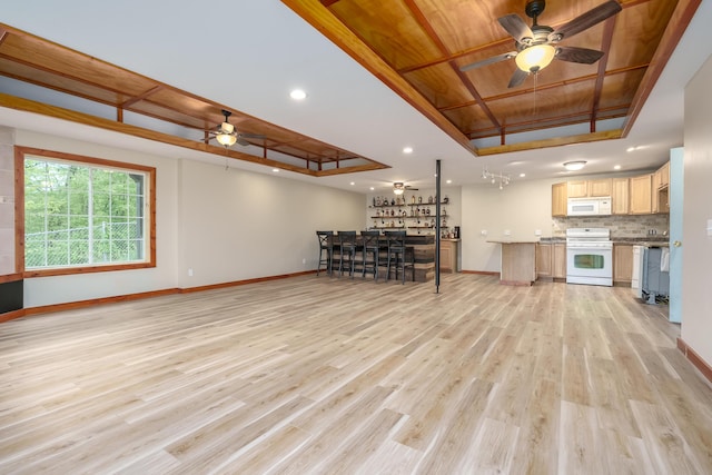 unfurnished living room featuring light wood finished floors, a tray ceiling, a ceiling fan, and baseboards