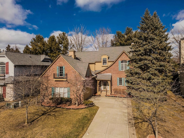 view of front of home with brick siding, concrete driveway, a front yard, a balcony, and a chimney