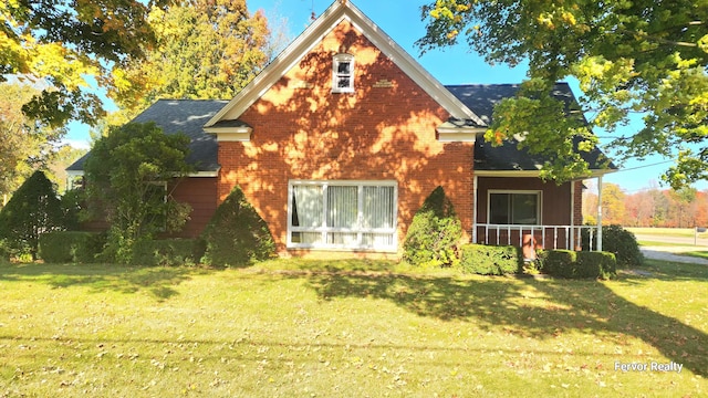 back of house with covered porch, roof with shingles, brick siding, and a lawn