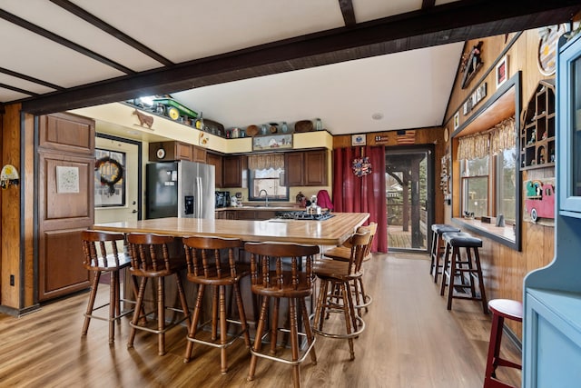 kitchen featuring beam ceiling, stainless steel fridge, light wood-style flooring, and a breakfast bar area