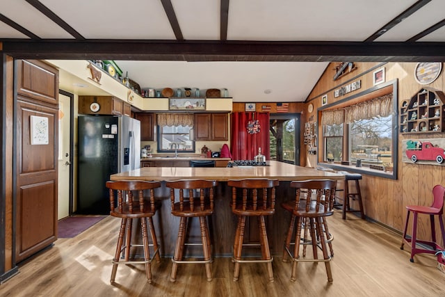 kitchen featuring a center island, vaulted ceiling with beams, light wood finished floors, stainless steel appliances, and wooden walls