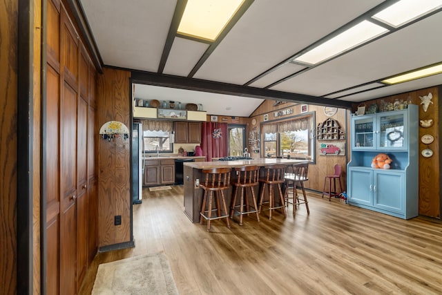 kitchen featuring wood walls, vaulted ceiling, light countertops, dishwasher, and light wood finished floors