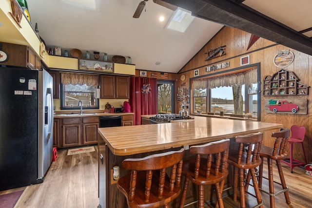 kitchen featuring vaulted ceiling with beams, stainless steel refrigerator with ice dispenser, wood walls, a sink, and wood finished floors