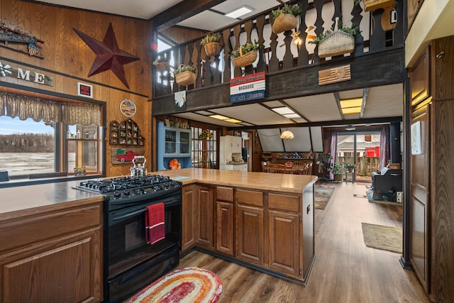 kitchen with black gas range oven, plenty of natural light, wooden walls, and wood finished floors