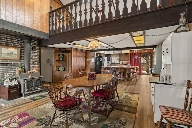 dining area with a wood stove, brick wall, wood finished floors, and beamed ceiling