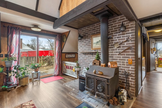 interior space with brick wall, beam ceiling, wood finished floors, and a wood stove