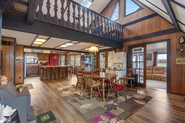 dining space with wood finished floors, a high ceiling, french doors, wood walls, and a notable chandelier