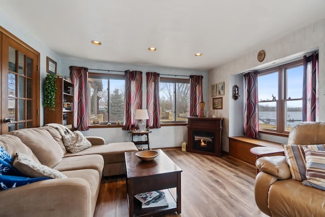 living area with a warm lit fireplace, baseboards, wood finished floors, and recessed lighting