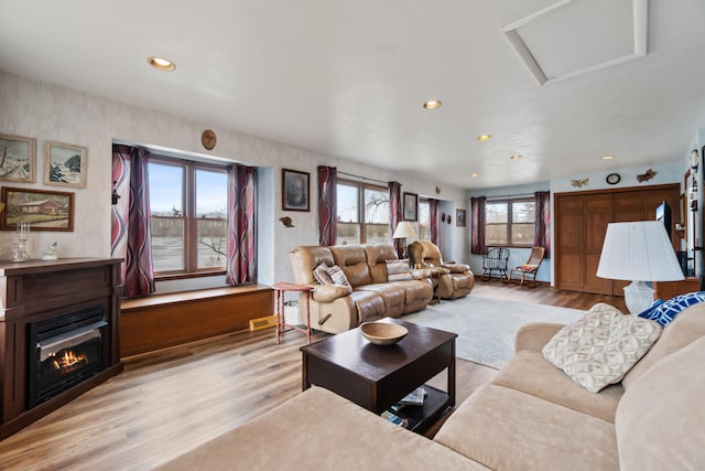 living area featuring light wood finished floors, a glass covered fireplace, attic access, and recessed lighting