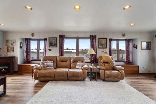 living area with a warm lit fireplace, recessed lighting, wood finished floors, and a healthy amount of sunlight