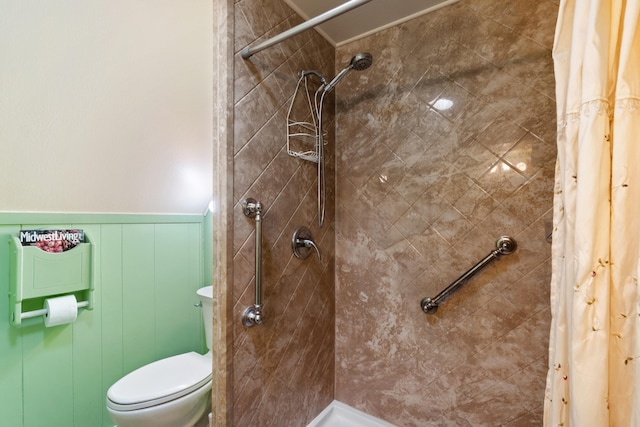 bathroom with a wainscoted wall, tiled shower, and toilet