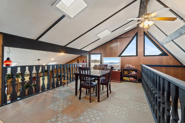 interior space featuring wood walls, lofted ceiling with skylight, and a ceiling fan