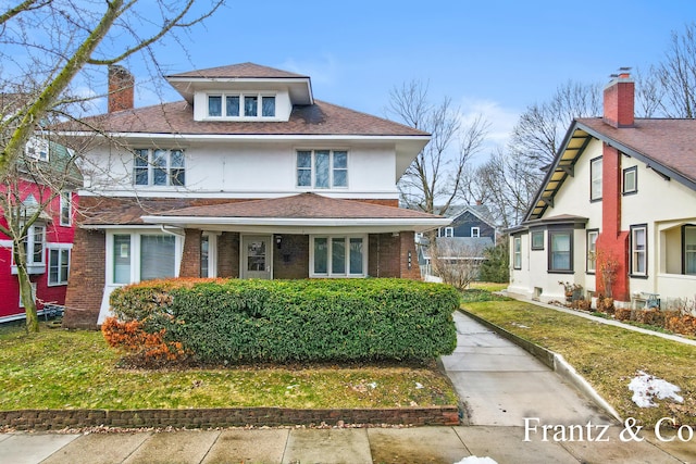 american foursquare style home featuring stucco siding, brick siding, a chimney, and a front yard