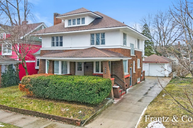 american foursquare style home with brick siding, a detached garage, roof with shingles, stucco siding, and an outdoor structure