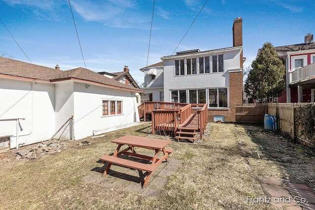 back of property with stucco siding, fence private yard, a chimney, and a wooden deck