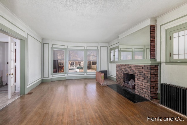 unfurnished living room with a fireplace, a textured ceiling, radiator heating unit, and wood finished floors