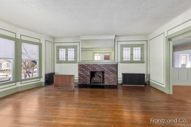 unfurnished living room with a decorative wall, radiator, a fireplace, and wood finished floors