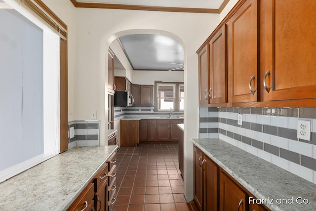 kitchen featuring light stone counters, arched walkways, a sink, dark tile patterned floors, and backsplash